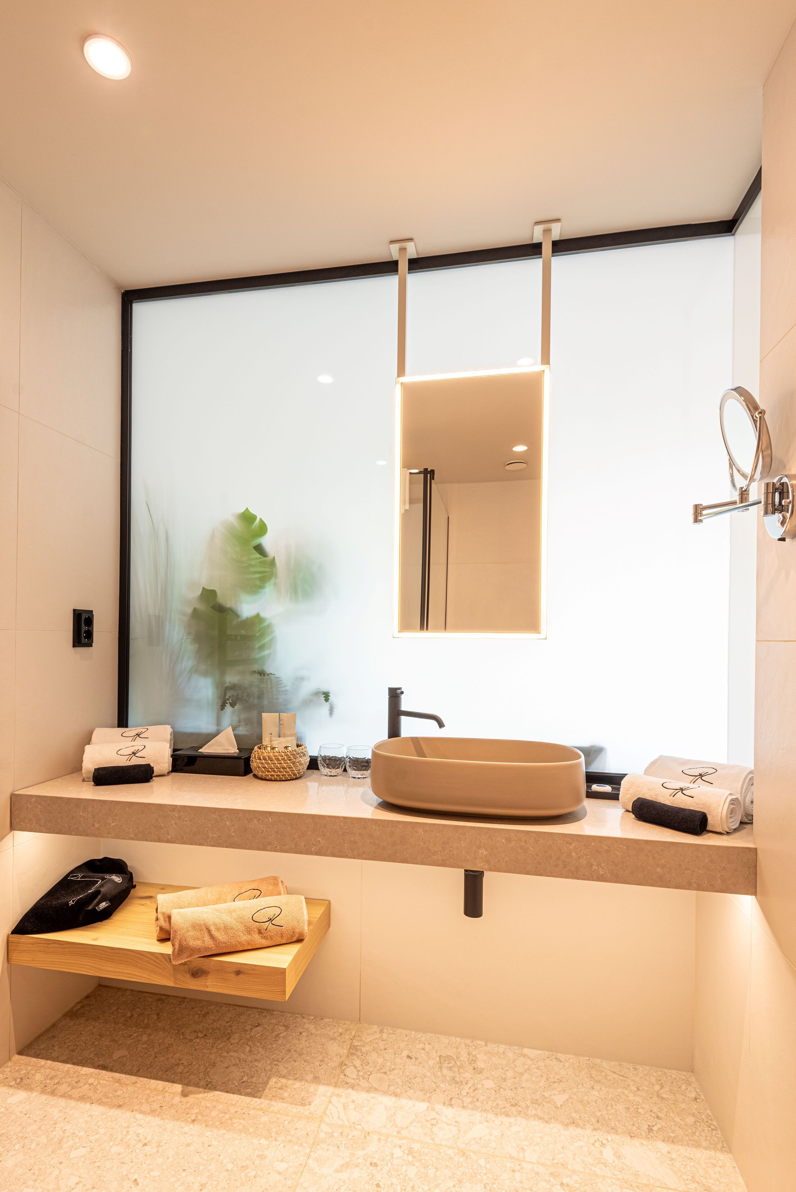 Un baño moderno con un espejo grande, un lavamanos redondo y un estante de madera con toallas.