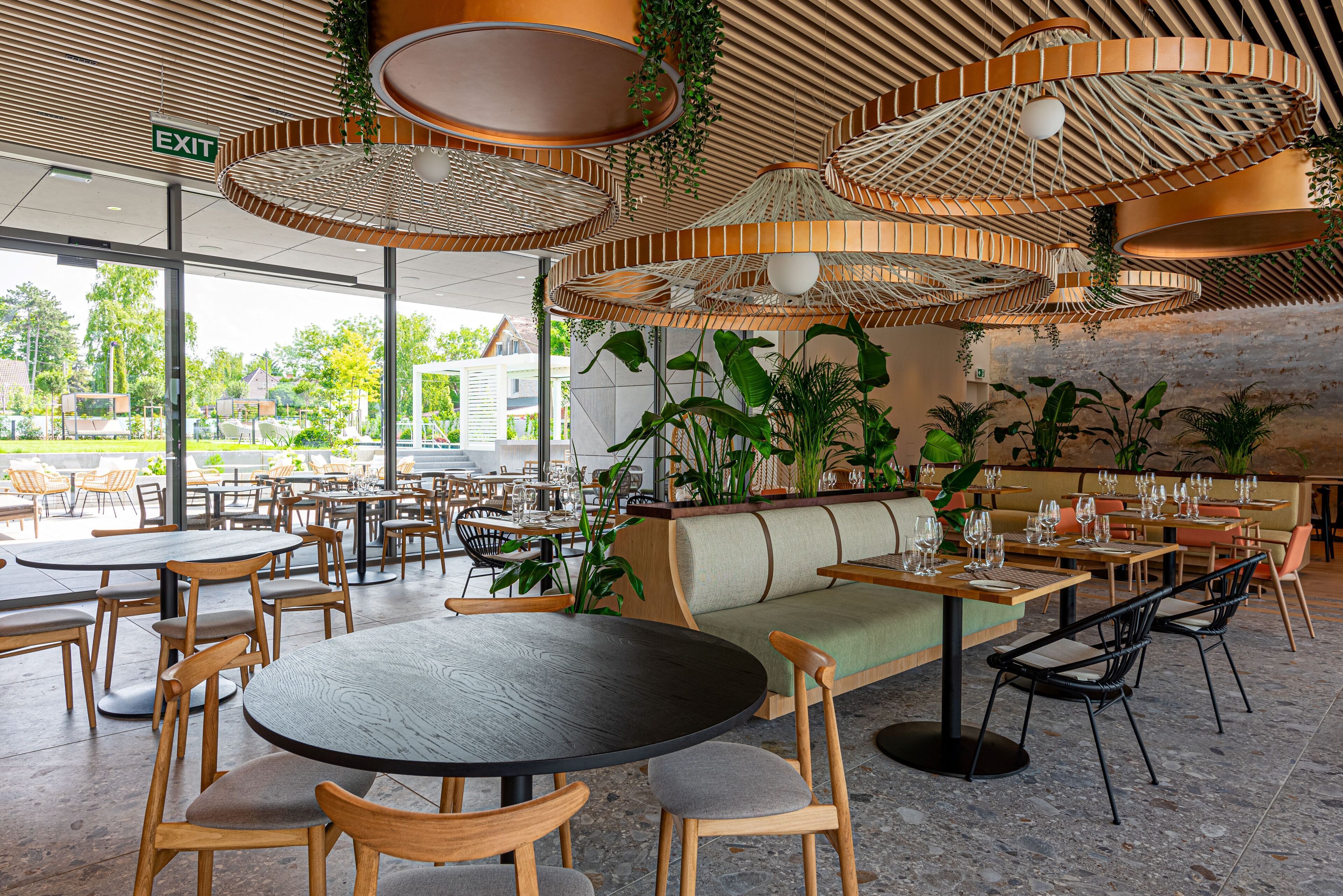 A restaurant with round tables, wooden chairs, and hanging wicker lamps.
