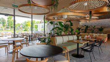 A restaurant with round tables, wooden chairs, and hanging wicker lamps.