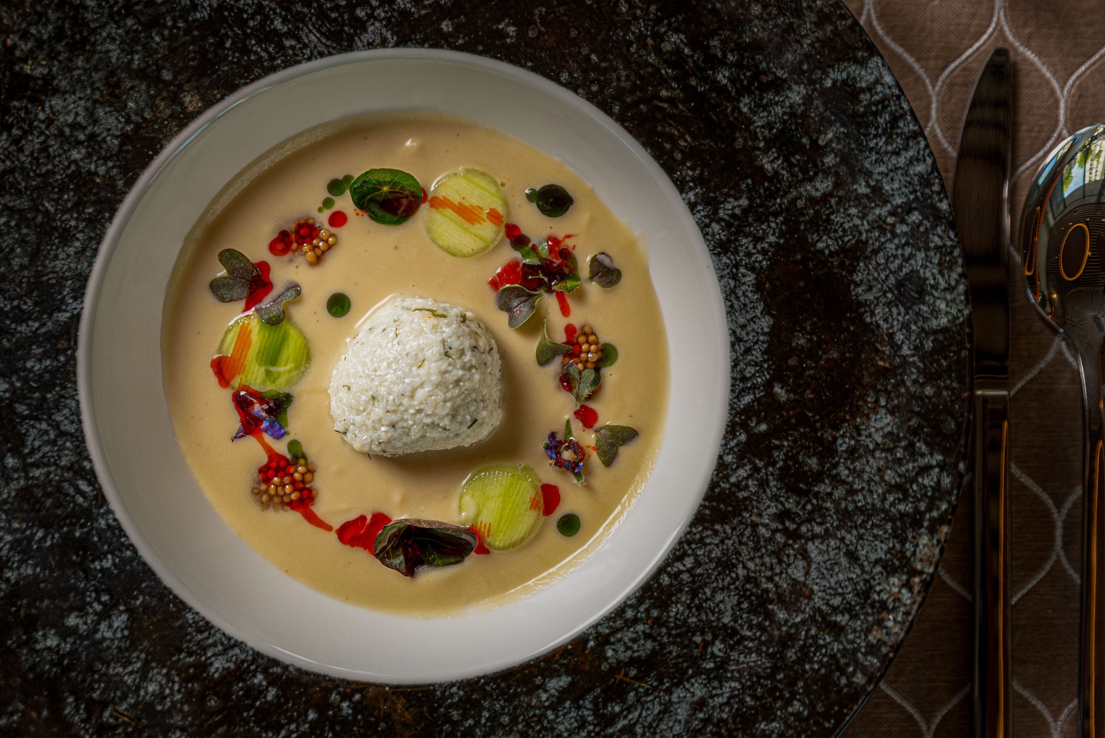 A bowl of food with a creamy sauce, garnished with various colorful toppings.