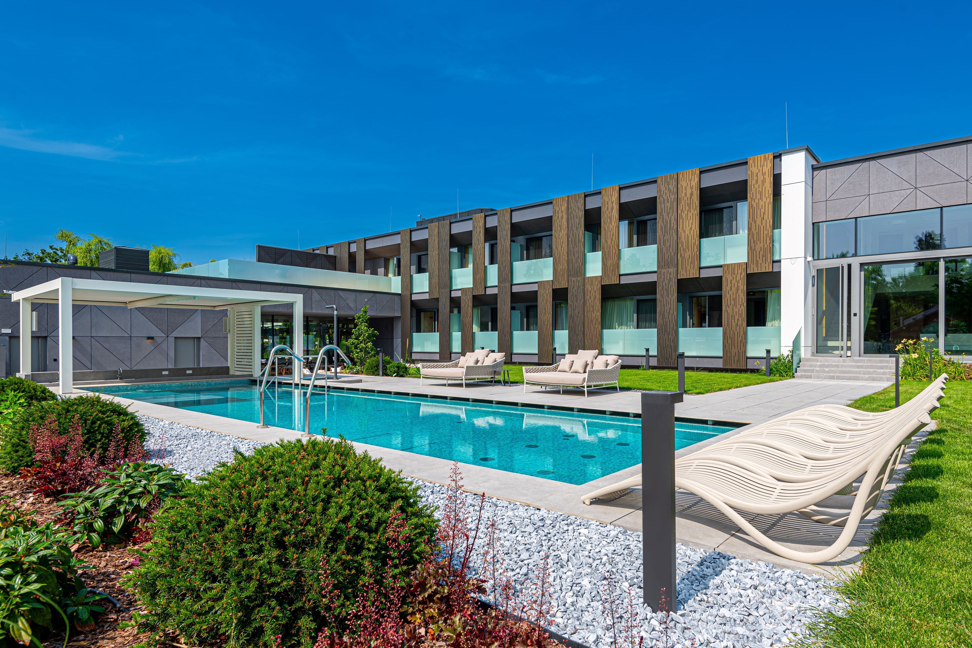 Un bâtiment moderne doté d’une piscine, de chaises longues et d’un patio couvert.