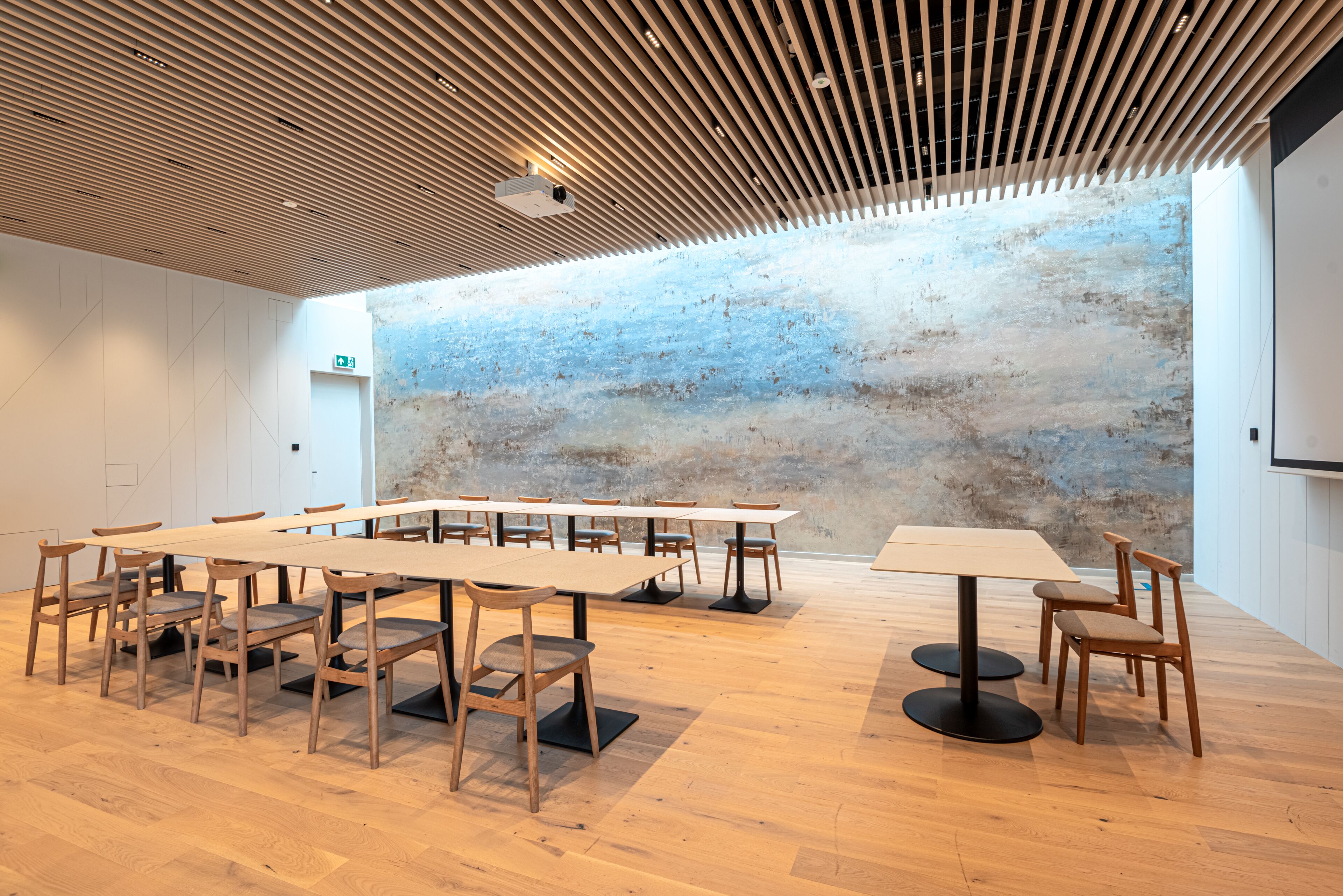 A conference room with a long table and chairs, a projector, and a textured wall.