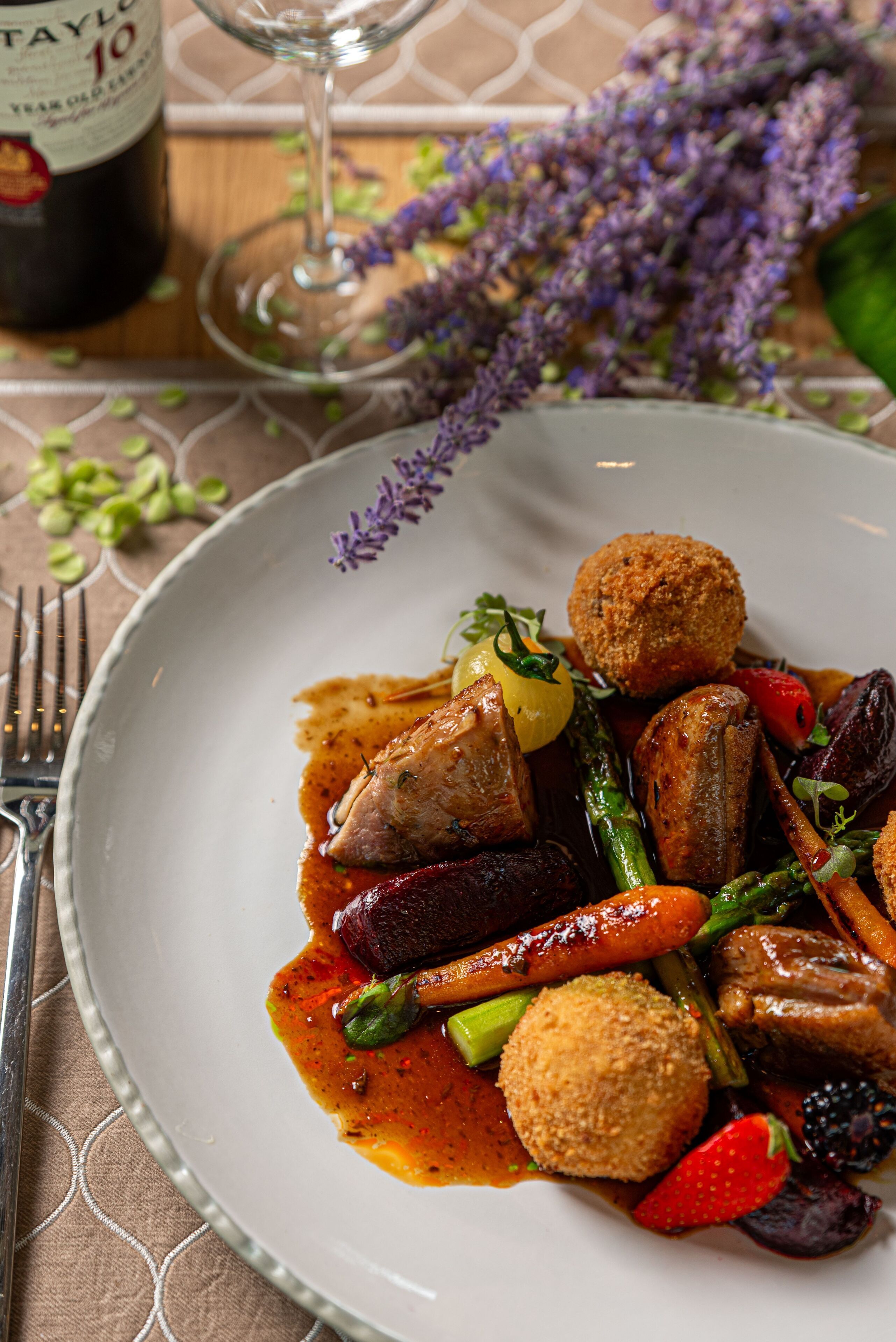 A plate of food with various vegetables and meat, a wine bottle, and a glass of wine on a table.