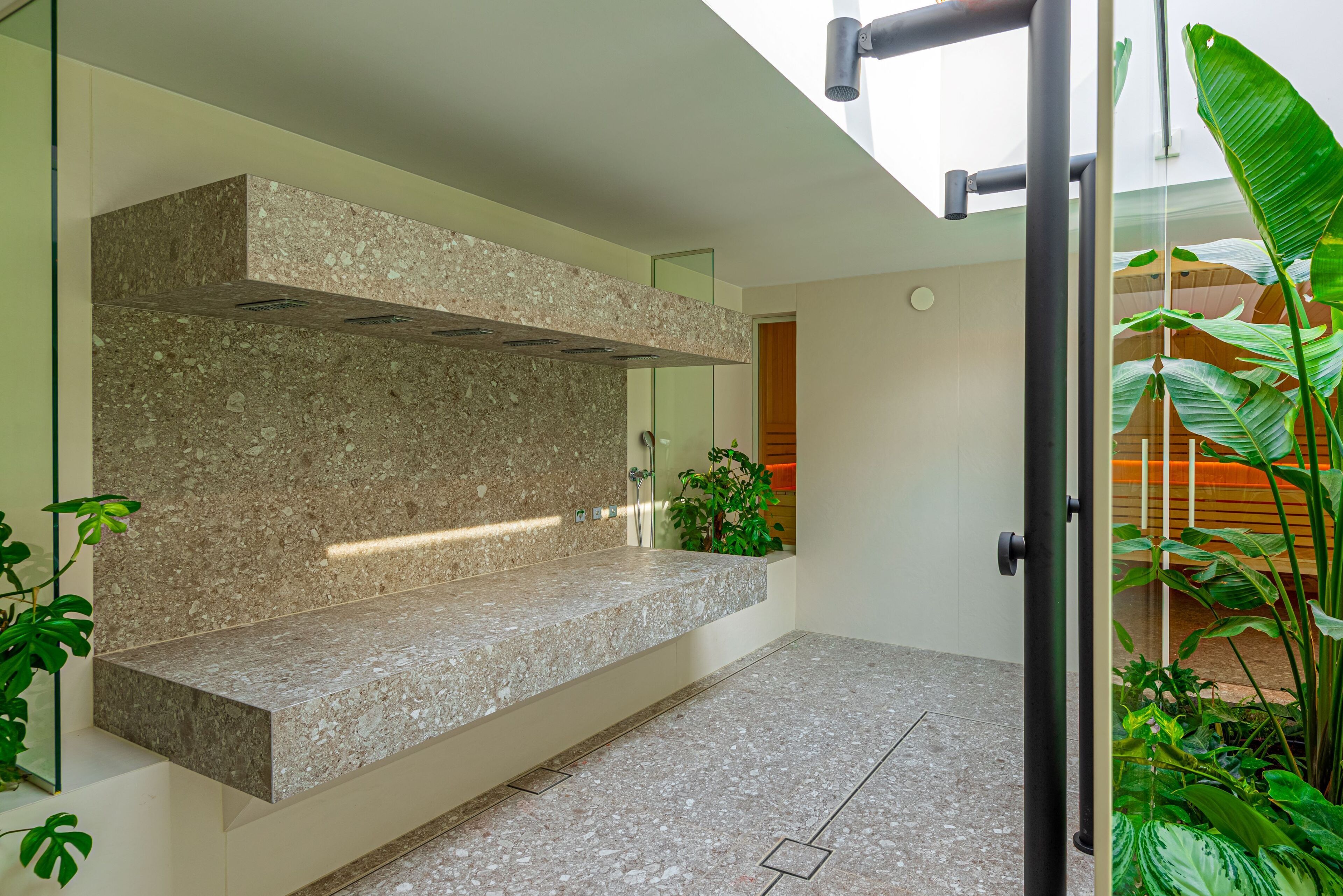 Un baño moderno con encimera de granito, cabina de ducha de vidrio y vista a un jardín exuberante.