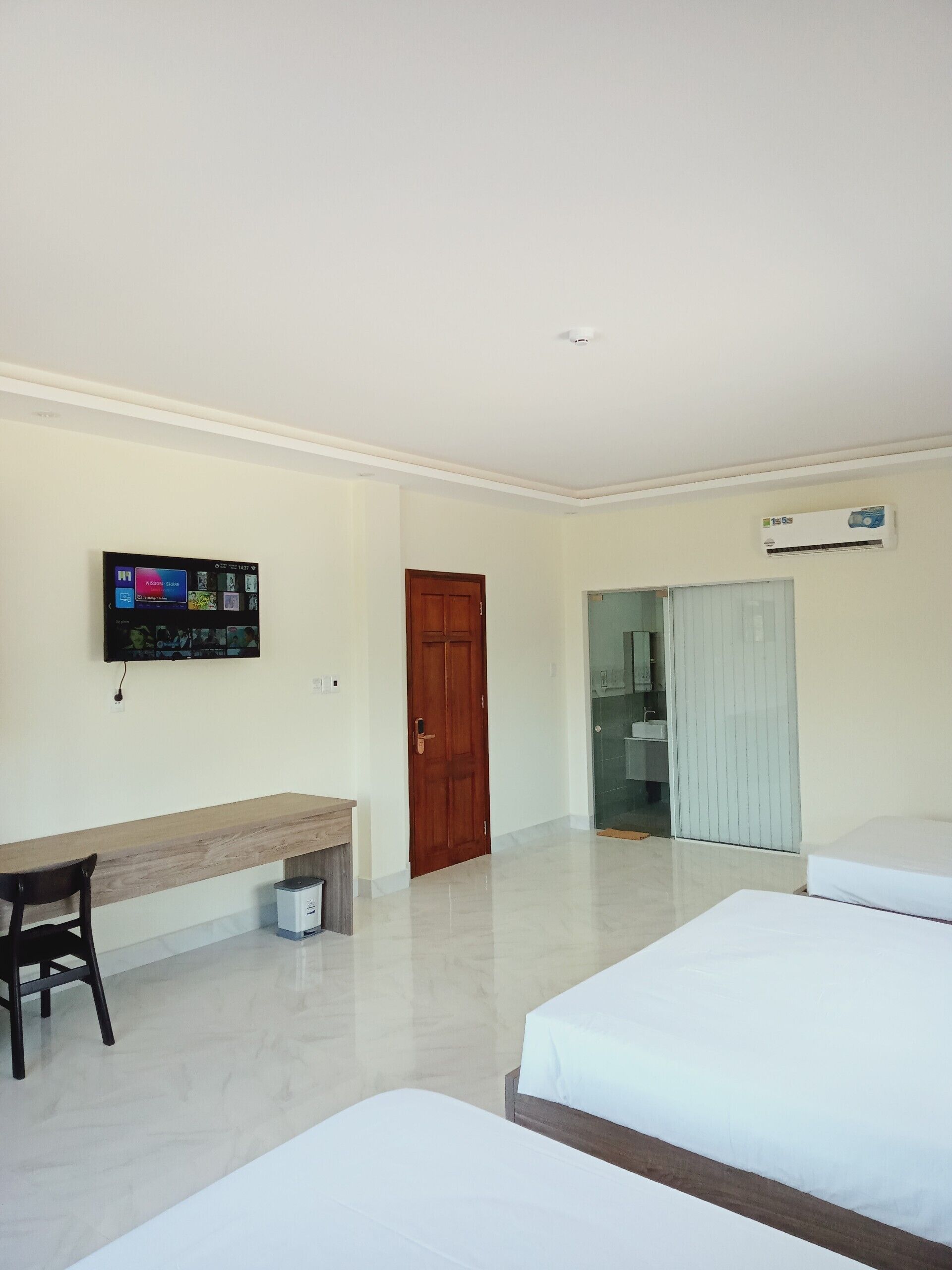 Habitación de hotel con una cama, un escritorio, una silla, un televisor montado en la pared y una puerta que da a un baño.