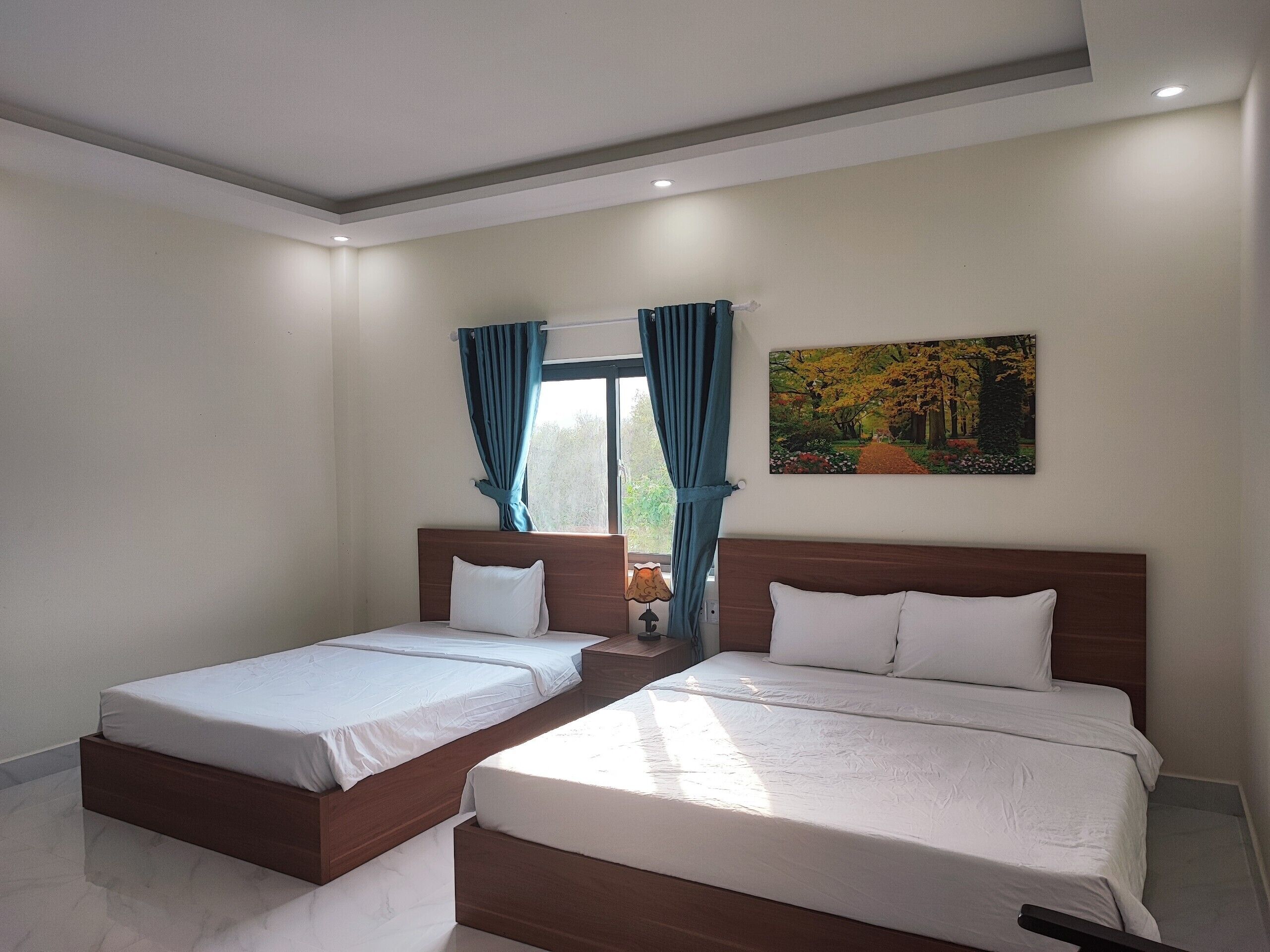 Een slaapkamer met twee bedden, een raam met gordijnen, een schilderij aan de muur en een lamp op een nachtkastje.