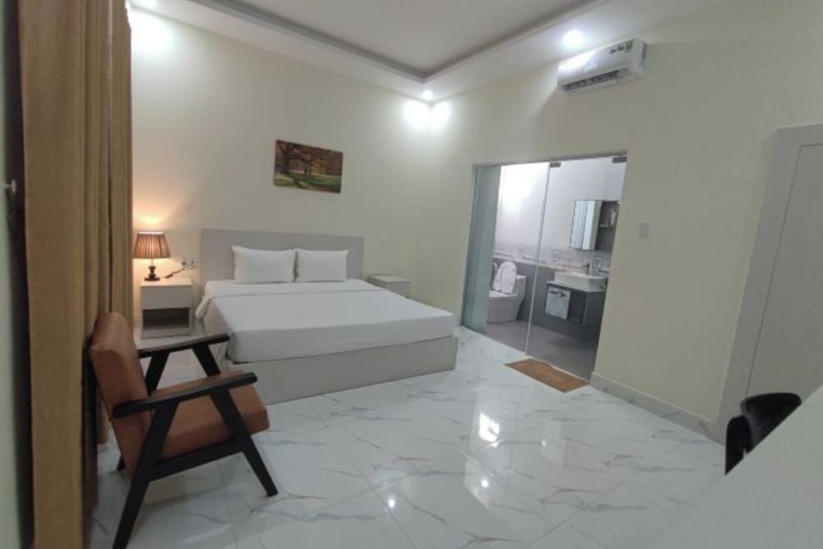 A hotel room with a bed, a chair, a desk, a lamp, and a bathroom visible through an open door.