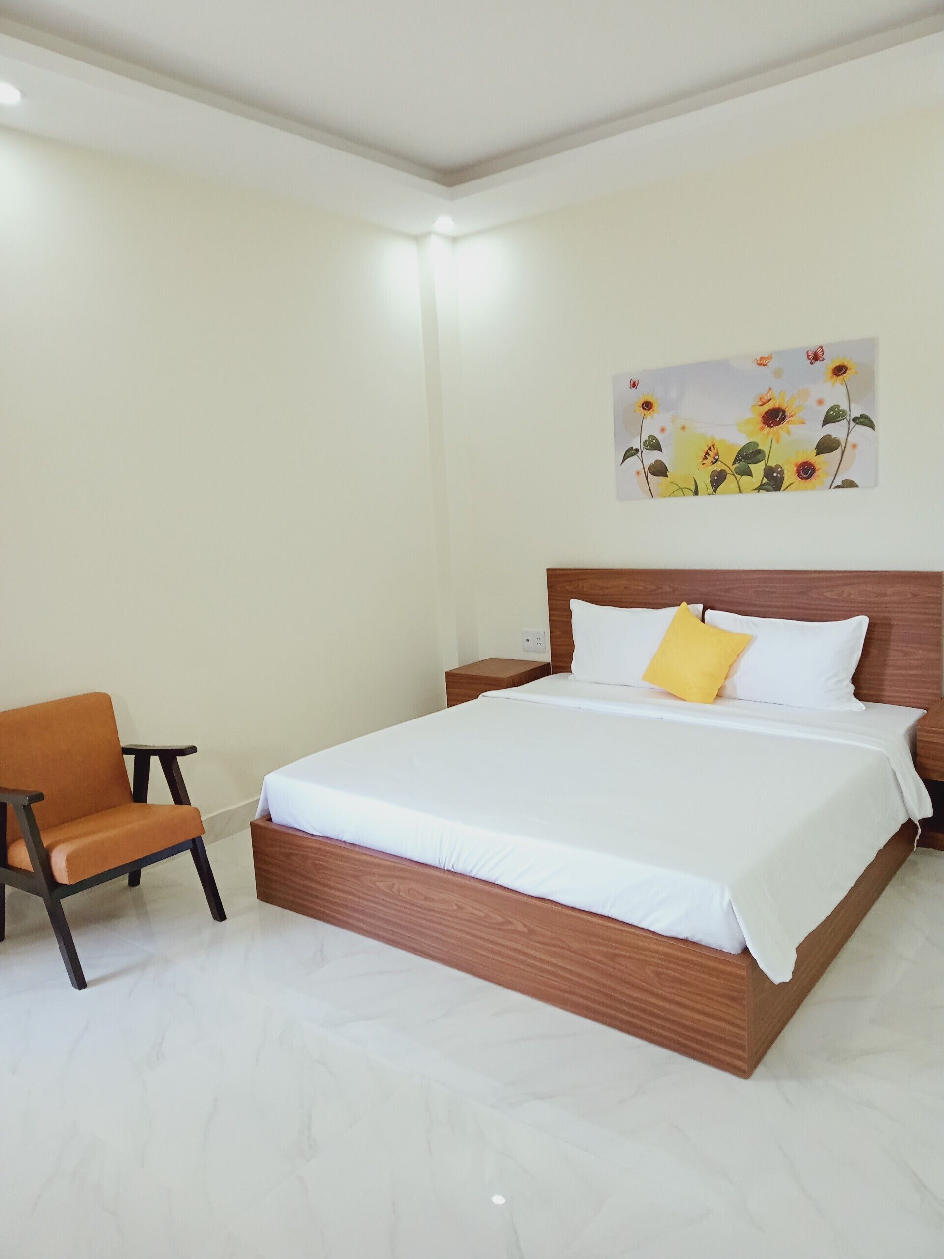 A bedroom with a wooden bed, white bedding, a single orange chair, and a wall-mounted artwork of flowers.