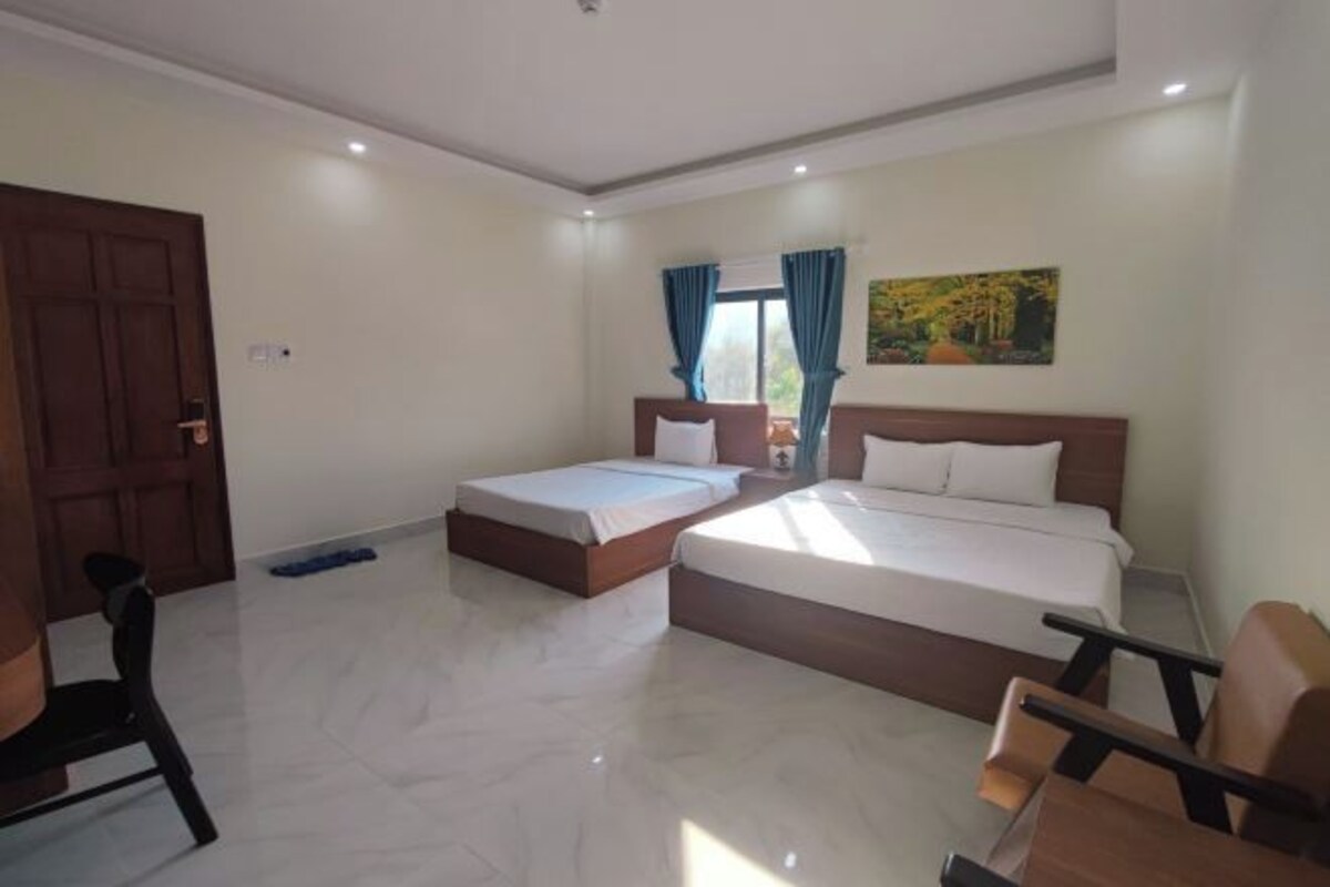 A hotel room with two beds, a wooden door, a painting on the wall, and a chair.