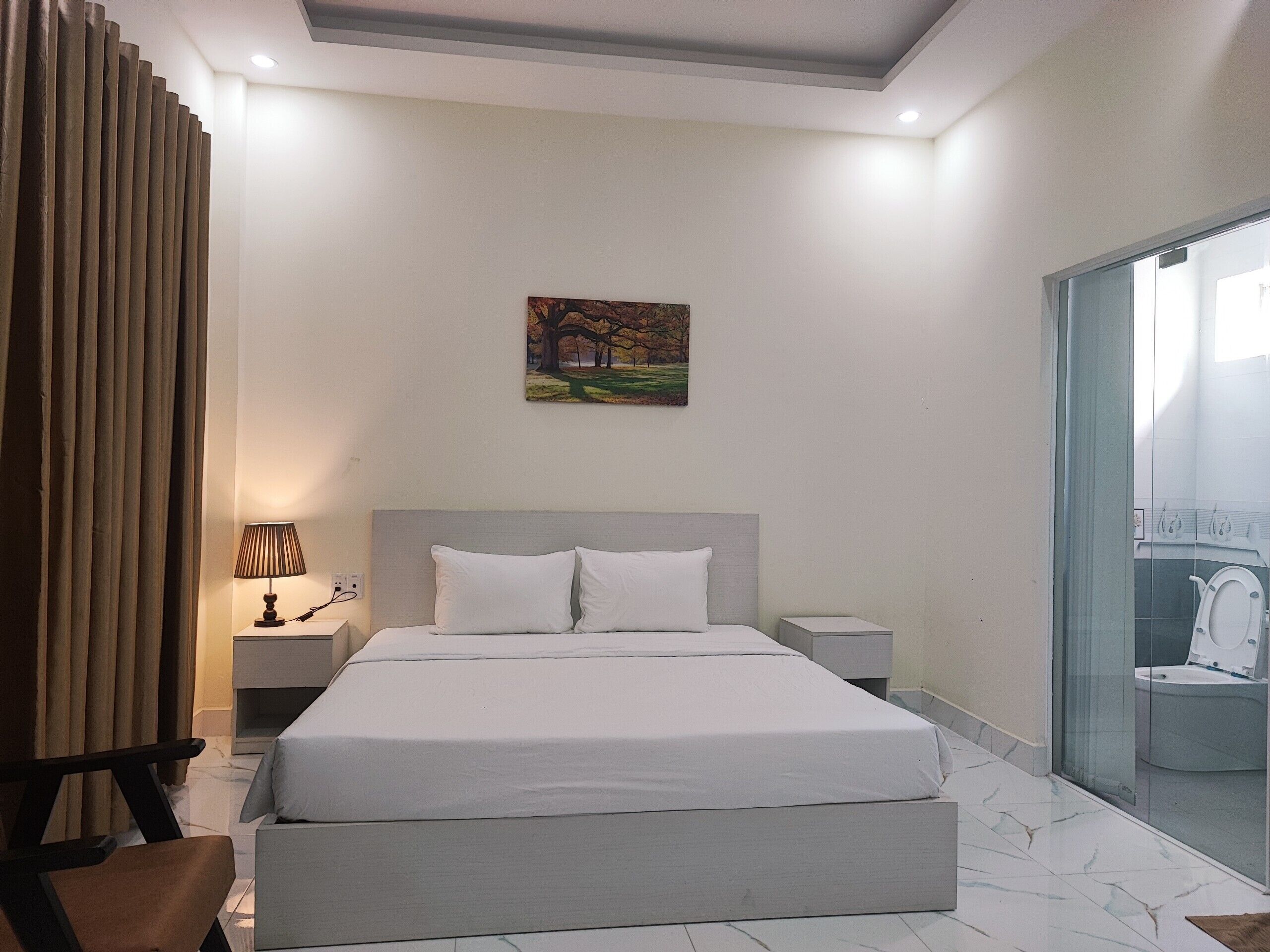 Een moderne slaapkamer met een groot bed, een nachtkastje, een lamp en een schilderij aan de muur.