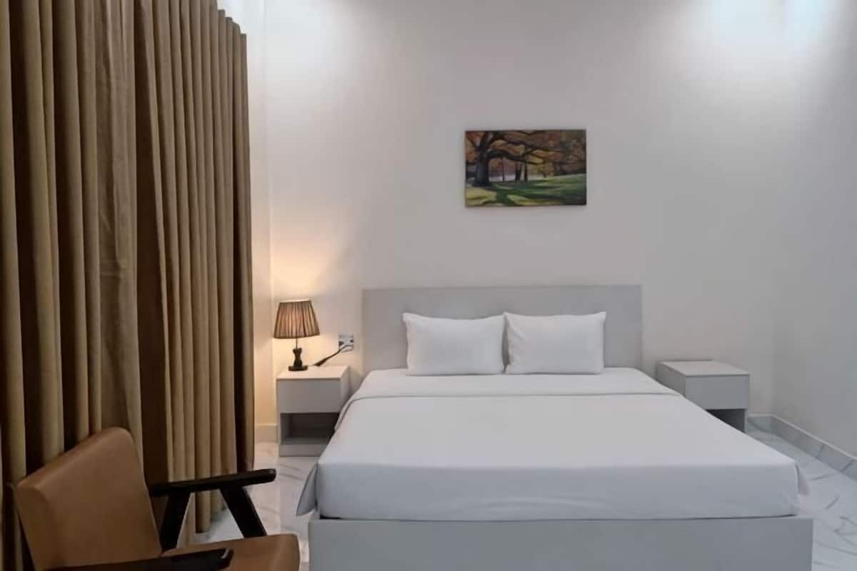 A hotel room with a bed, a nightstand, a lamp, a chair, and a painting on the wall.