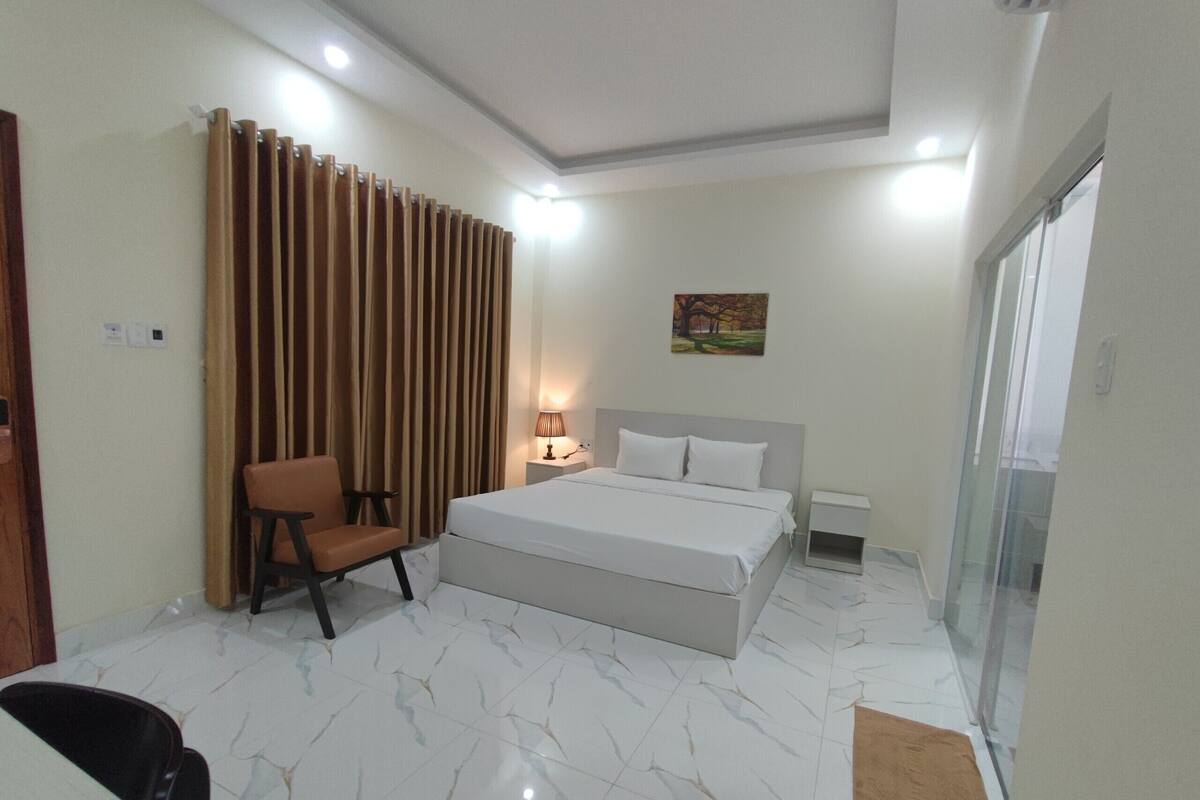 A hotel room with a bed, a chair, a lamp, and a painting on the wall.