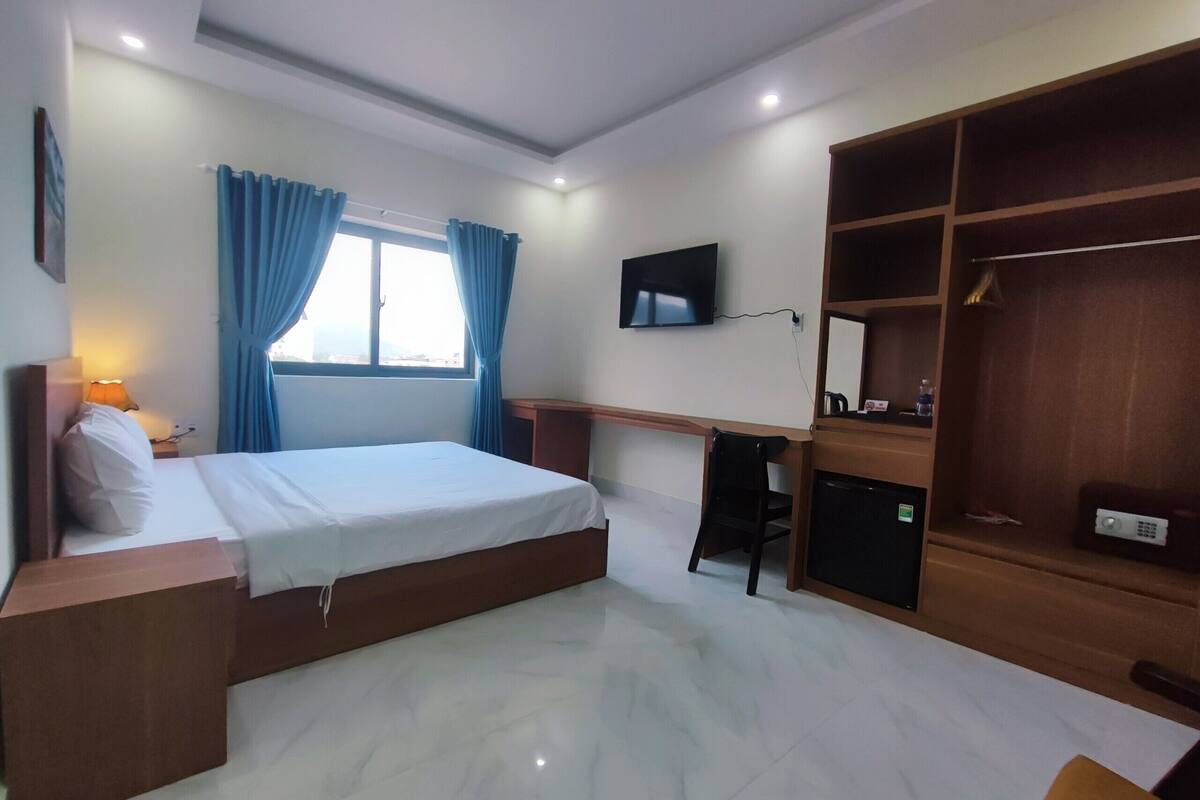 A hotel room with a bed, desk, chair, TV, and wardrobe.