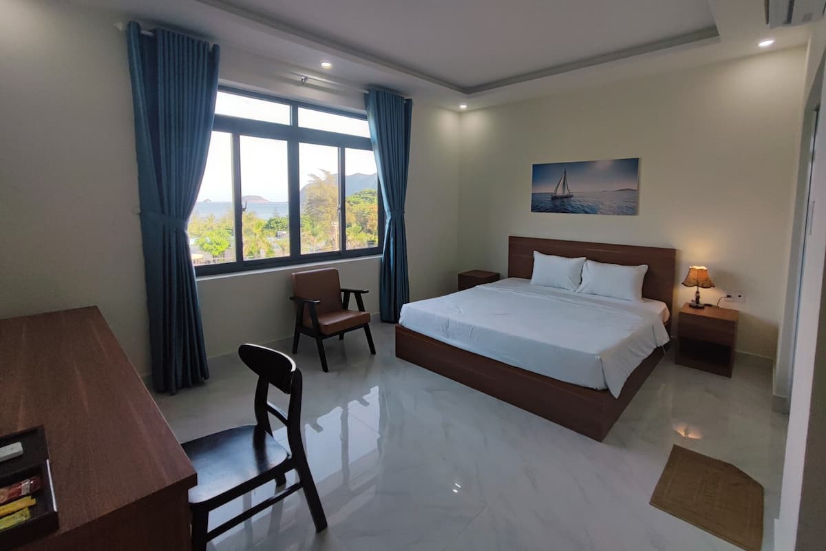 A hotel room with a bed, a desk, a chair, a nightstand, and a window with curtains.