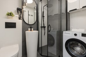 A modern bathroom with a glass shower enclosure, a built-in washing machine, and a toilet.