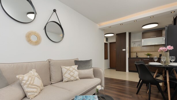 Una sala de estar moderna con un sofá, una mesa de comedor con sillas y una zona de cocina al fondo.