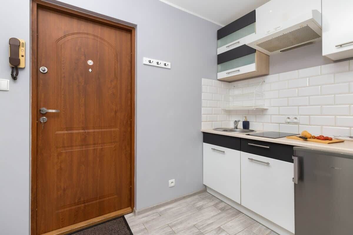 A compact kitchen with white cabinets, a wooden door, and a countertop with a cutting board and vegetables.