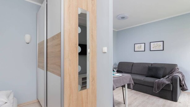 A modern room with a grey sofa, a dining table with a glass top, and a wooden sliding door.