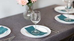 A table set with white plates, teal napkins, and clear wine glasses, with a vase of flowers in the background.
