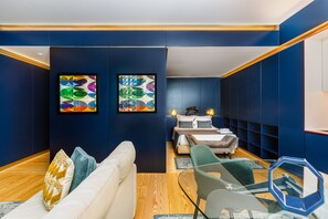 A modern hotel room with a dark blue wall, a white sofa, a green armchair, and a bed with a nightstand. - Náutico Deluxe Apartment by APT IIN Cascais Center (Cascais)