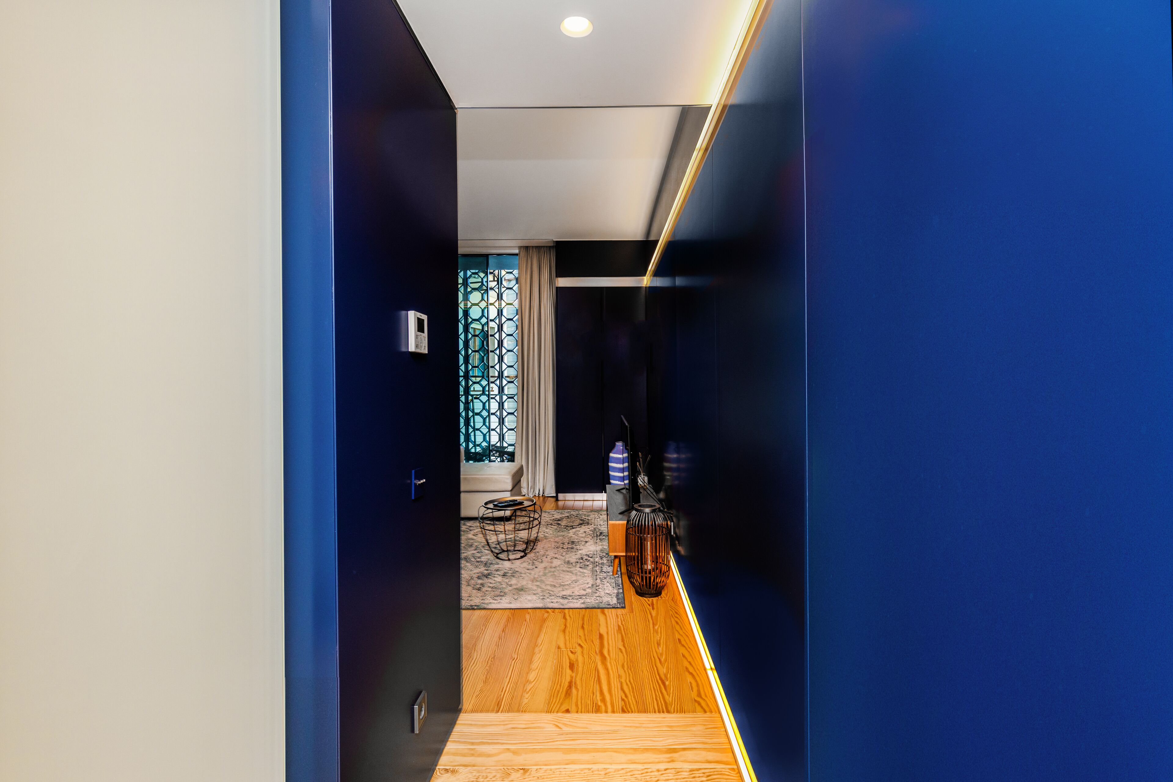 A modern hallway with a wooden floor, a blue accent wall, and a decorative metal railing.
