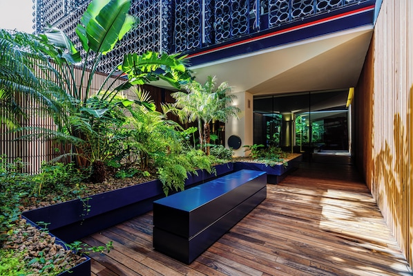 A modern outdoor space with wooden decking, black planters with greenery, and a contemporary building with a geometric facade.
