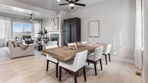 Un vaste espace de vie comprenant une table à manger, des chaises blanches, un canapé et un ventilateur de plafond.