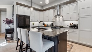 Une cuisine moderne avec des armoires blanches, un îlot central et une hotte de cuisine en acier inoxydable.