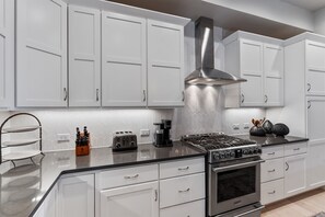 Eine moderne Küche mit weißen Schränken, einer Edelstahl-Dunstabzugshaube, einem Gasherd, einem Toaster und einer Kaffeemaschine.