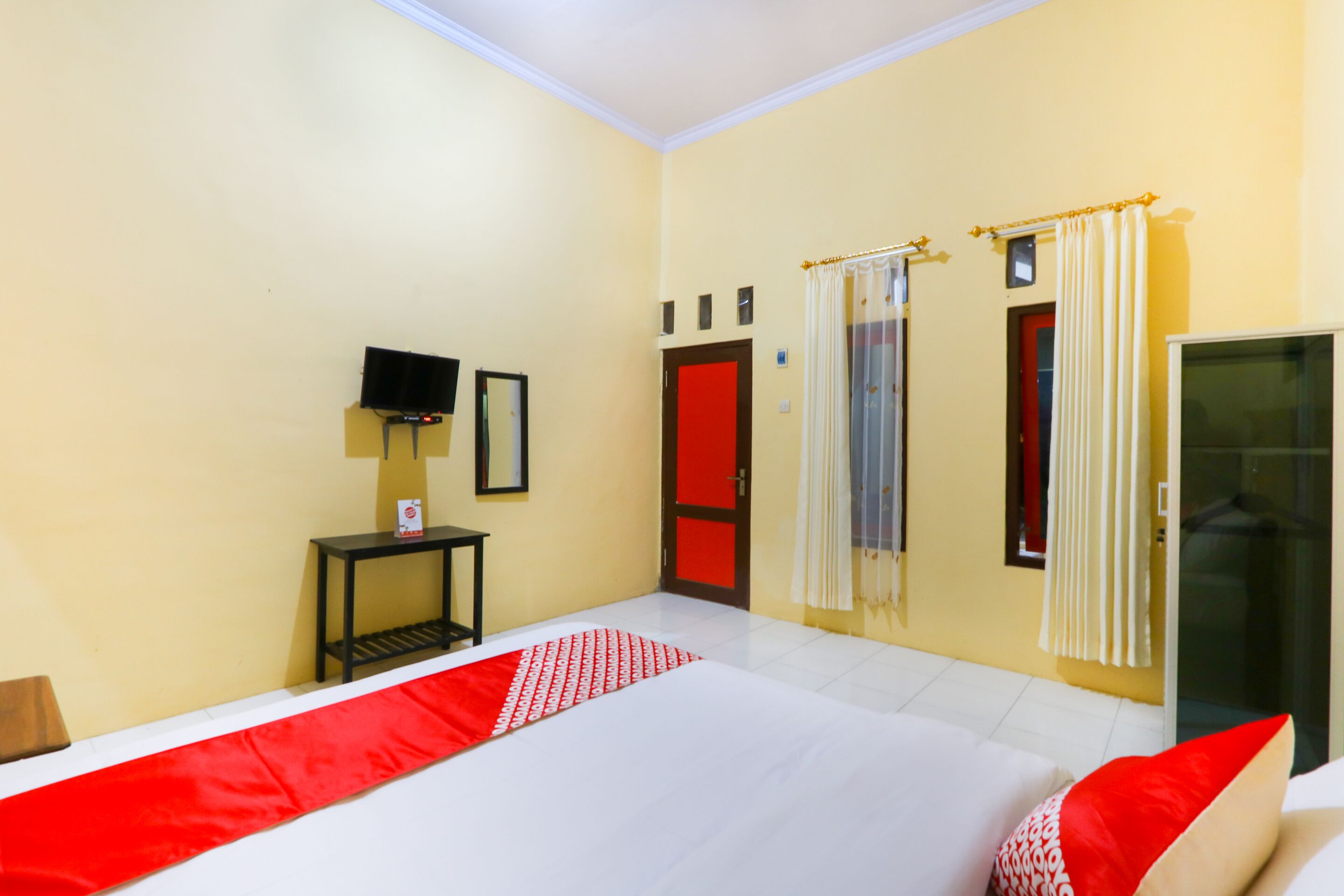 A hotel room with a bed, a TV on a stand, a small table, and a door with a red frame.