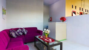 A living room with a purple sofa, a glass coffee table, and a vase with flowers. - Hotel O El Shaday Family Residence (Banyuwangi)