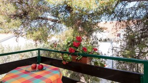 Een balkon met een geruit tafelkleed, een rieten stoel en een bloempot met rode bloemen.