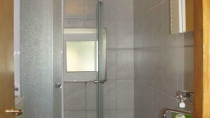 Een badkamer met een douchecabine van glas, een wastafel met zeepdispenser, en een spiegel boven de wastafel.