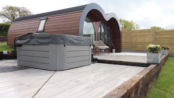 A modern outdoor patio with a hot tub, a wooden deck, and a seating area with a chair and a table.