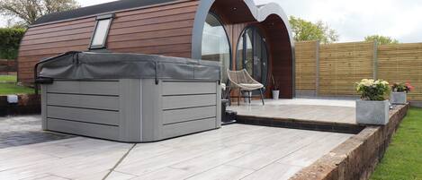 En moderne udendørs terrasse med jacuzzi, træterrasse og siddeområde med stol og bord.