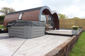 A modern outdoor patio with a hot tub, a wooden deck, and a seating area with a chair and a table. - Ceunant (Aberystwyth)