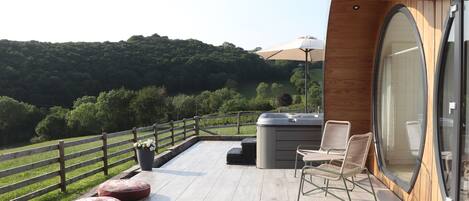 A wooden deck with a hot tub, seating, and a view of a green landscape.