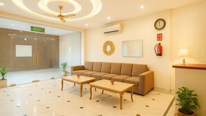 A hotel lobby with a sofa, two wooden tables, a ceiling fan, a clock, and a fire extinguisher. - OPO THE ALPINO (New Delhi)