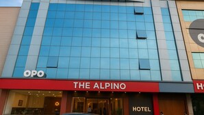 A hotel with a prominent 'THE ALPINO' sign, a large glass facade, and an 'OPO' sign on the left. - OPO THE ALPINO (New Delhi)
