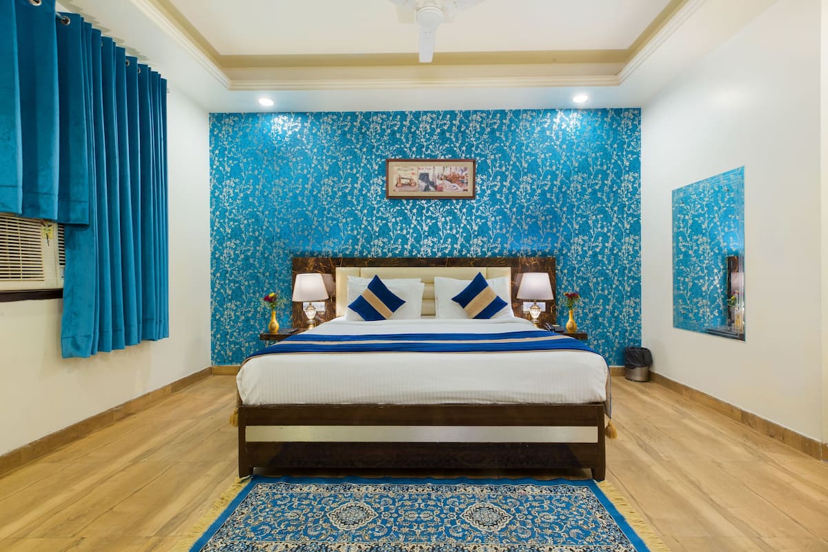 A bedroom with a bed, a blue patterned wall, a wooden floor, and a blue curtain.