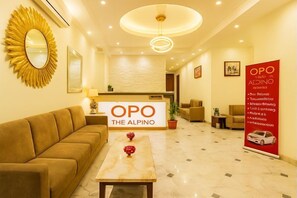 A hotel lobby with a reception desk, a sofa, a coffee table, a mirror, and a chandelier. - OPO THE ALPINO (New Delhi)