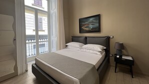 A hotel room with a bed, a nightstand, a lamp, a painting, and a view of the outside balcony. - Relais Ranieri (Naples)