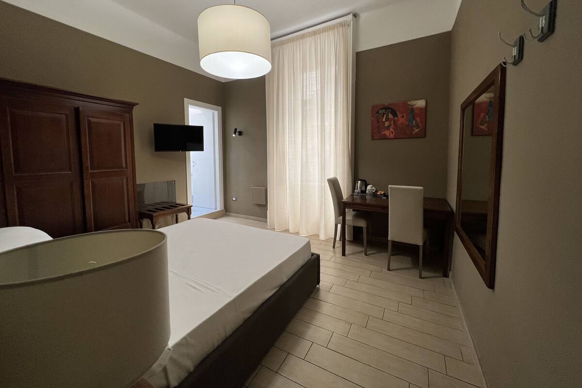 A hotel room with a bed, a desk, a chair, a television, and a large mirror.
