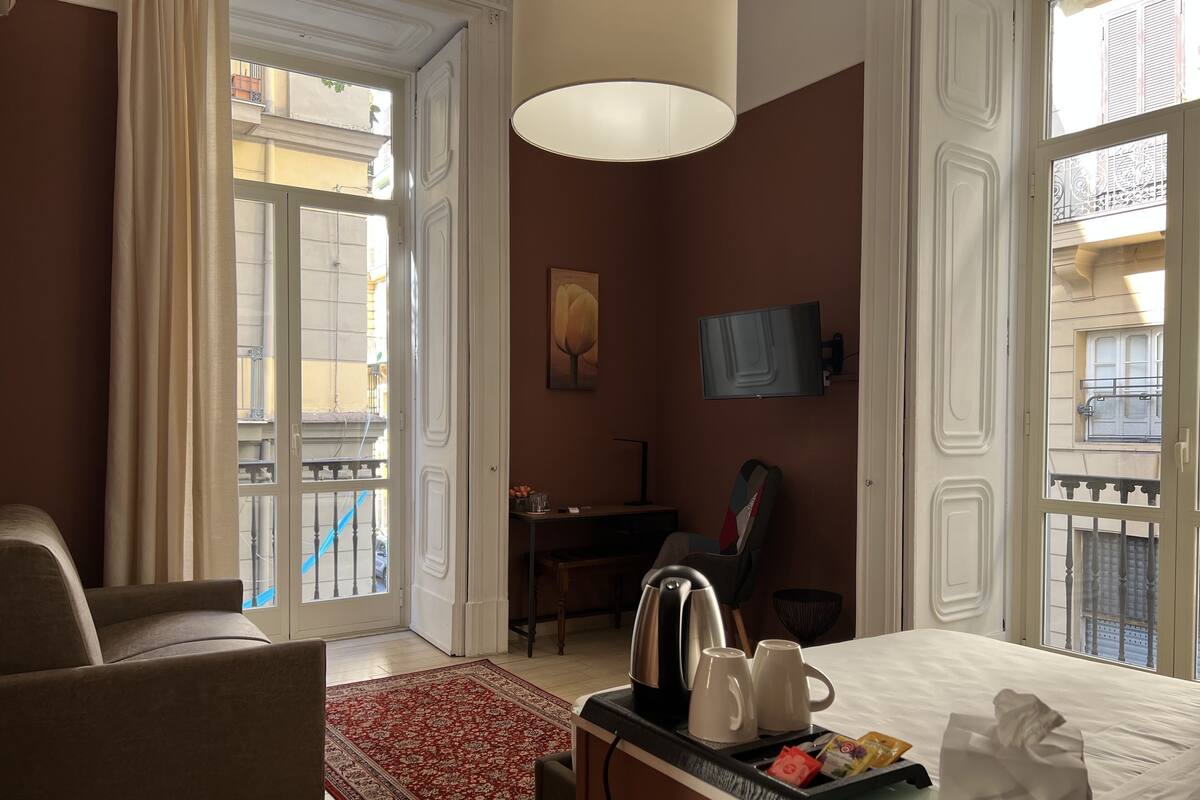 A hotel room with a bed, a desk with a chair, a coffee maker, a TV, and a view of the outside balcony.