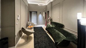 A modern hallway with a dark green sofa, a small round table, and a chair. There is a door labeled "104" in the background. - Relais Ranieri (Naples)