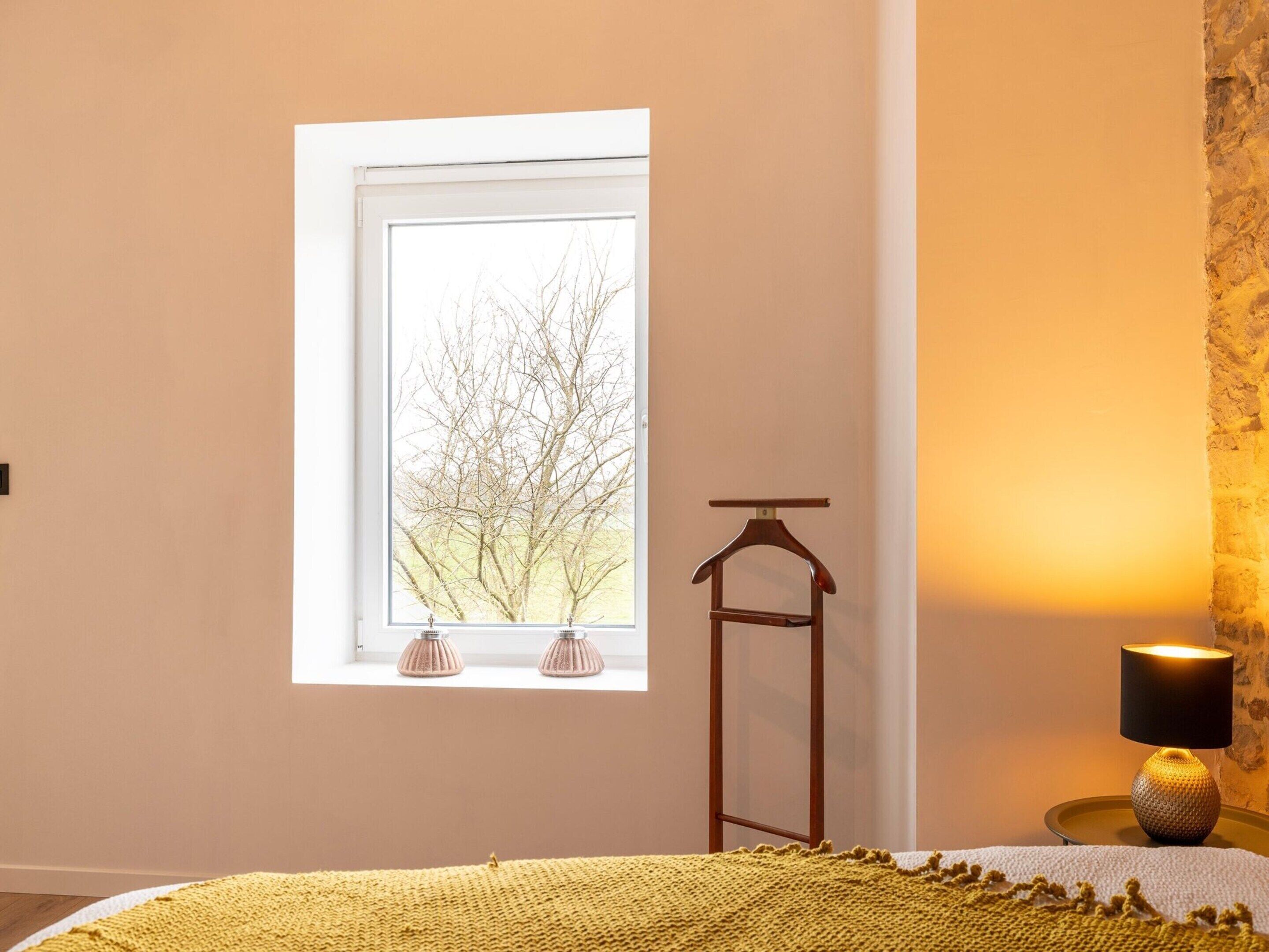 Un dormitorio con ventana, una mesita de noche con lámpara y una cama con colcha amarilla.