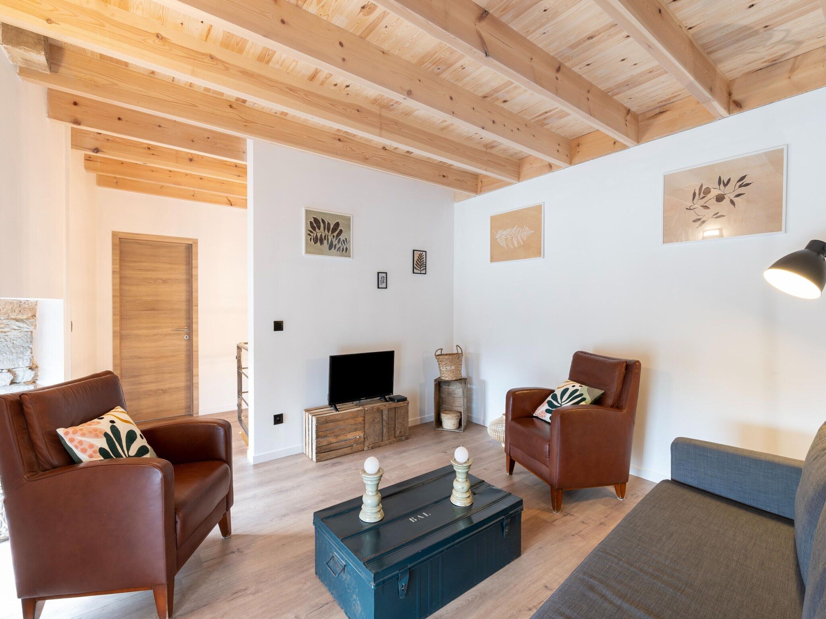 A cozy living room with wooden beams, a fireplace, and a television.