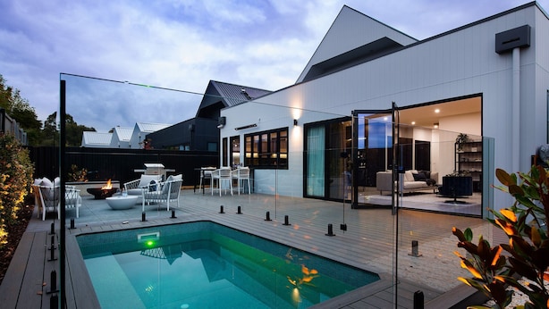 A modern outdoor pool area with a glass enclosure, a fire feature, and outdoor seating.