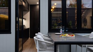 A modern dining area with a dark wooden table, white wicker chairs, and a fruit platter.