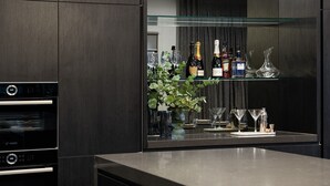 A modern kitchen with a built-in Bosch oven, a glass shelf displaying various bottles and glasses, and a potted plant.